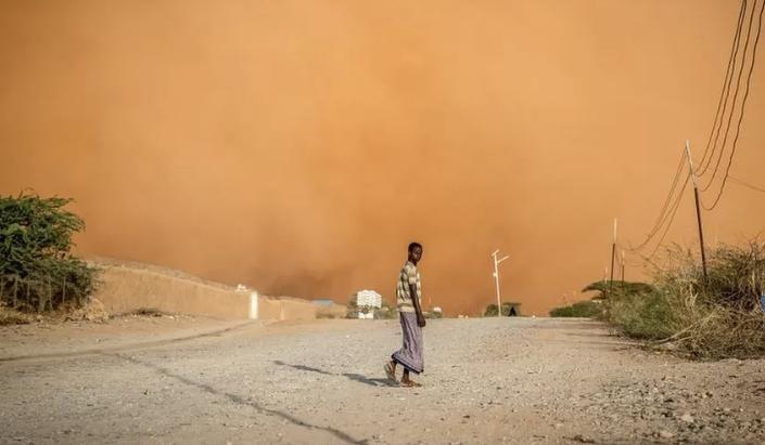 A man walks in front of a sandstorm in Dollow, southwest Somalia